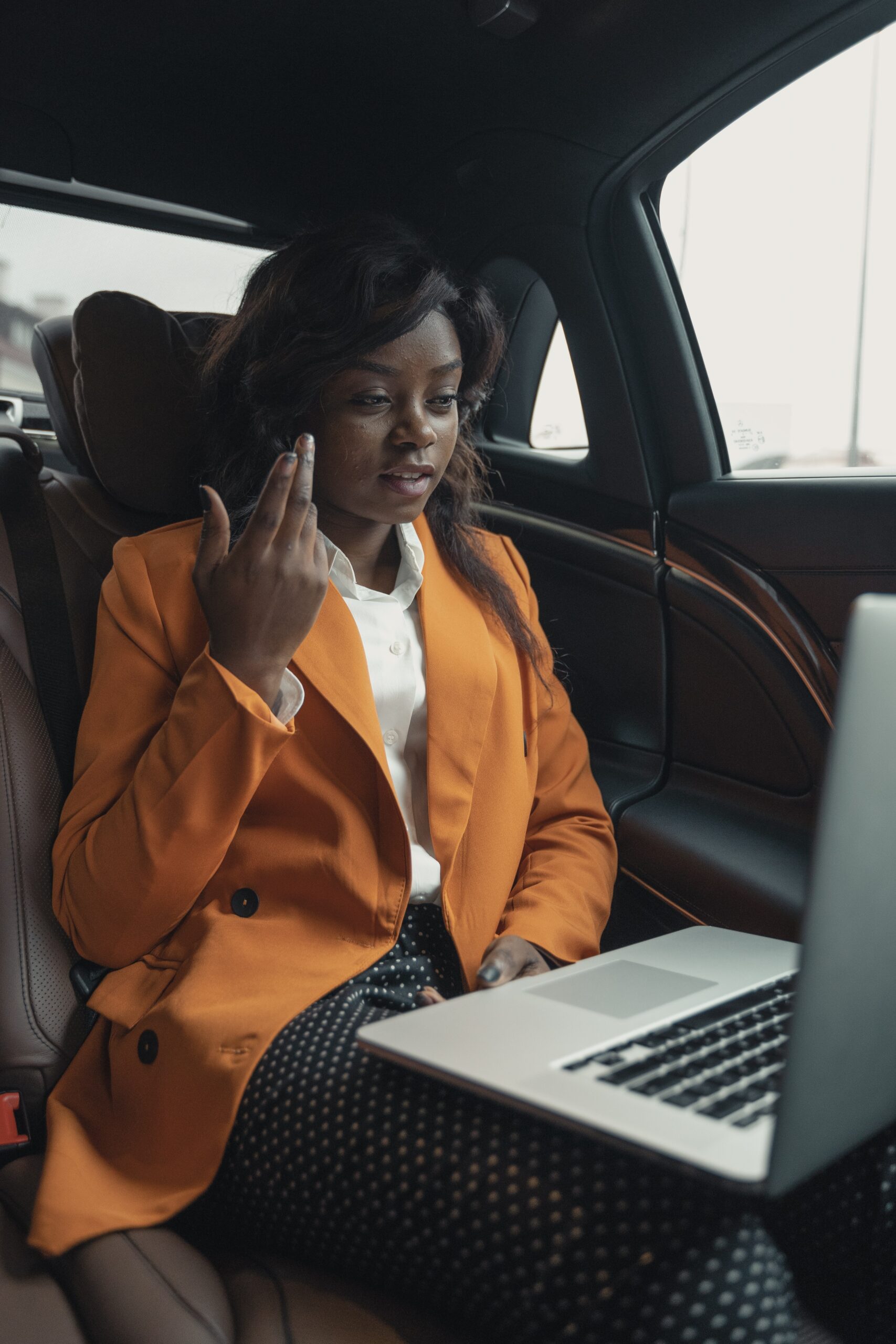 woman in a suit jacket sitting in the back of a car while on a conference call on laptop